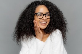 Joyful young woman with curly hair and glasses laughing on a gray background
