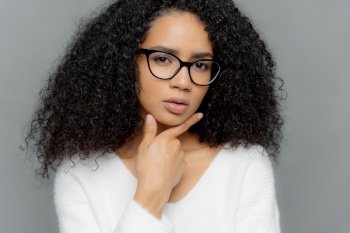 Thoughtful woman with curly hair and glasses on a grey background