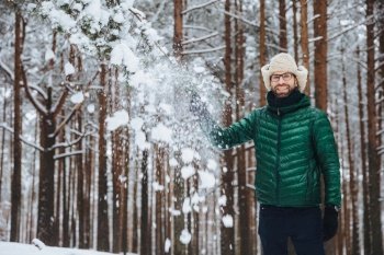 Man in winter forest touching snow-covered branch, joyful and content