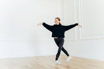 Energetic woman dancing in a black crop top and leggings, spacious white room, expressing joy and freedom in movement
