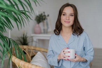 Serene woman in a striped pajama top with a mug, relaxed indoor setting with green plants, embodying tranquil home life