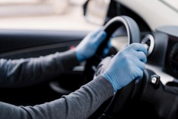 Driver’s hands on a steering wheel, wearing blue protective gloves for hygiene