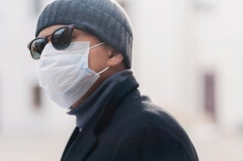 Profile of a person outdoors wearing sunglasses and a surgical mask for health safety