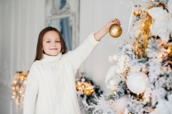 Smiling girl decorating Christmas tree with golden baubles, festive mood