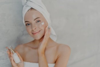 Smiling woman with towel on head applying serum for glowing skin