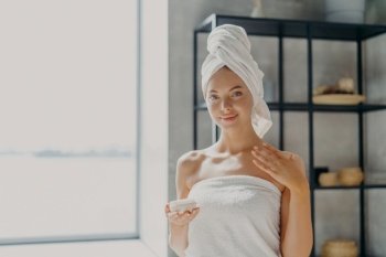 Elegant woman with a towel on her head holding a skincare product