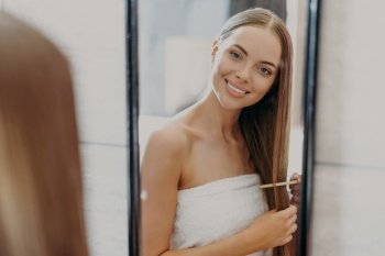 Smiling woman with smooth hair wrapped in a towel looking in mirror.. Smiling woman with smooth hair wrapped in a towel looking in mirror