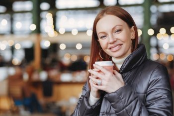 Smiling redhead woman enjoying coffee in urban cafe setting