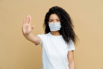Woman with face mask gesturing stop, white shirt, neutral background