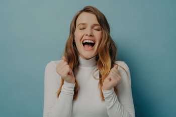 Exuberant young woman in white turtleneck laughing with eyes closed, full of joy and vivacity against a serene blue backdrop