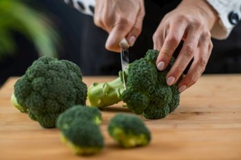 Cutting fresh organic broccoli, a superfood rich in vitamin K, vitamin C, folic acid, potassium, phytonutrients, and fibers.