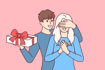 Groom surprises girlfriend standing with gift box and covering girl eyes with hand. Boyfriend in love congratulates happy bride on birthday and Christmas or valentine day on february 14th.. Groom surprises girlfriend standing with gift box and covering girl eyes with hand