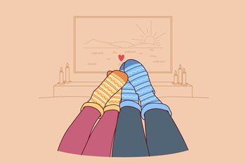 Feet of loving couple in autumn warm socks lying on sofa and watching TV in romantic home atmosphere. Couple spending time together and enjoying comfort during autumn weekend or vacation. Feet of loving couple in autumn warm socks lying on sofa and watching TV in romantic home atmosphere