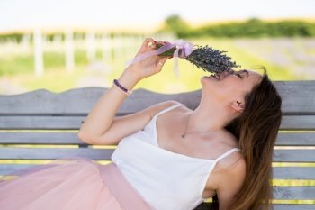 a beautiful girl in a dress with a bouquet of lavender flowers sits on a bench