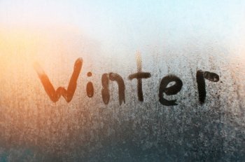 Winter text on frozen window. Frosty pattern on glass, sunny morning. Sunshine