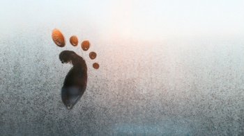 Drawing of a child’s foot on a frozen window, copy space. Frosty pattern on glass. Funny creative concept. Textured ice surface.