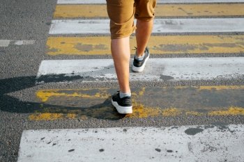 Rear view of a man in shorts and sneakers crossing the road on a pedestrian crossing, close-up of male legs. Selective focus