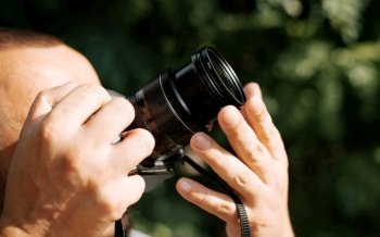 Close-up of a photographer holding a digital camera and photographing something outdoors on a sunny day. Side view of a man holding a lens, hobby concept. Unrecognizable person