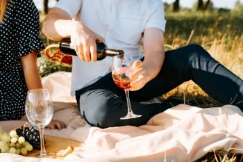 Family picnic in nature, couple love story. Close-up of man pouring red wine into wine glass for his girlfriend. Romantic date outdoors.. Family picnic in nature, couple love story. Close-up of man pouring red wine into wine glass for his girlfriend. Romantic date outdoors