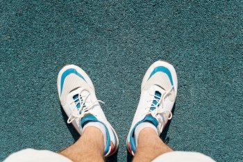 Top view sportsman in white sneakers stands on the rubber surface of the outdoor sports ground.