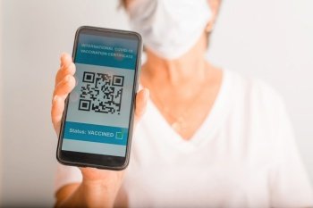 Elderly woman in protective medical mask showing electronic passport of a vaccinated person against covid-19, qr-code on screen of mobile phone, close-up. Selective focus on health passport Covid 19