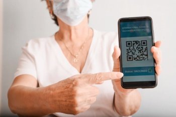 Health passport Covid 19. Close-up of elderly woman in protective medical mask points finger at the electronic passport of vaccinated Covid-19, qr code on screen of mobile phone