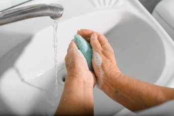 World hand washing day concept. Close-up of elderly woman washing her hands with soap in bathroom, disinfects, protects against bacteria and viruses.
