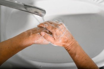 Close-up of an elderly woman washes her hands with soap and foam in sink, disinfects, protection from bacteria and viruses. World hand washing day concept.