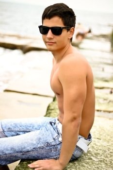 Young sexy man in sunglasses sitting on the beach
