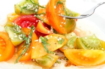 Different types of heirloom tomatoe wedges with thinly sliced basil leaves, sesame seeds and an olive oil and raspberry vinegar dressing. Heirloom Tomato Salad