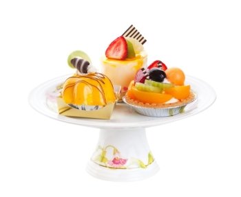 An assortment of Asian desserts, featuring (clockwise from top) Mousse Cake, Fruit Tart, and Mango Mousse.  Displayed on a pedestal cake plate and shot on white background.