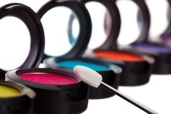 A colorful row of eyeshadow pots with a brush.  Shallow depth of field with focus on brush.