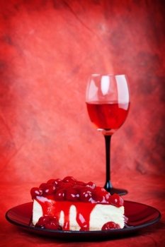 Decadent cherry cheesecake served on a candy apple red plate with red wine,on a red background.