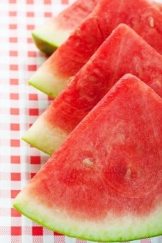 Four watermelon wedges on a red, checkered picnic table cloth.  Shallow depth of field.