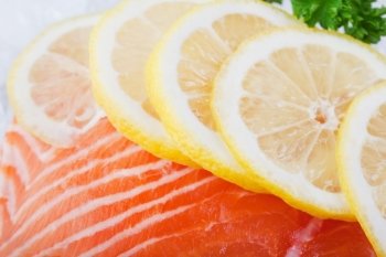 A salmon filet on ice with slices of lemon.