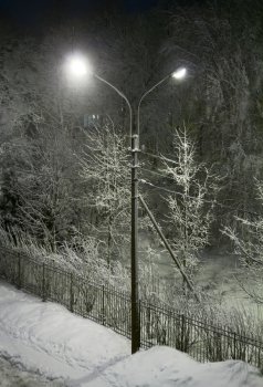 Winter street at night and shining lanterns through snowing. Night shot. Blue tone.