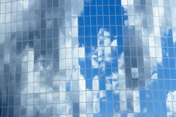 Blue sky with clouds reflected in glass windows of skyscrapers in the big mirror as