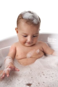  Baby girl is looking at bubbles in bathtub with foam on her head