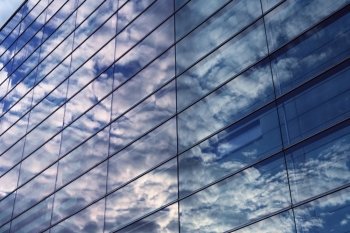 Sky and glass wall of an office building, reflections of clouds.