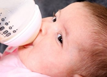 Cute face of Caucasian Hispanic baby, infant drinking milk out of bottle.