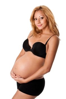 Beautiful new happy mother in late pregnancy wearing black panties and bra, holding belly, isolated.