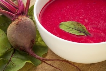a bowl of cream soup of red beets with a fresh beet root and leaves