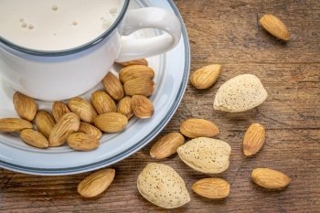 a cup of almond milk with almond nuts on a rustic barn wood table