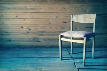 Vintage old wooden chair in grungy interior. Loneliness, estrangement, alienation concept. Toned image