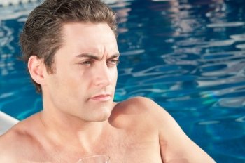 Close-up of young handsome man lost in thoughts near swimming pool