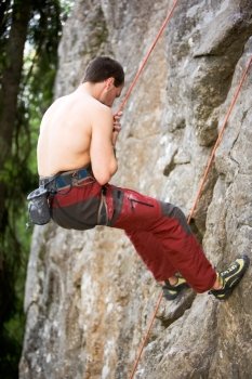 A male climber repells down a rock face - crag.