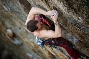 A male climber, viewed from above, climbs a very high and steep crag.