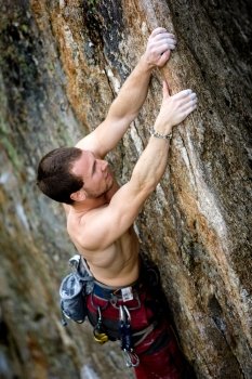 A male climber, viewed from above, climbs a very high and steep crag. 