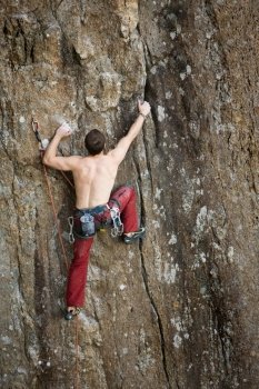 A male climber against a large rock face climbing lead against a magnificant landscape.