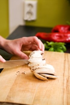 A detail image of a female hand slicing mushrooms for a pizza.  Shallow depth of field is used, with focus on the hands and mushrooms.